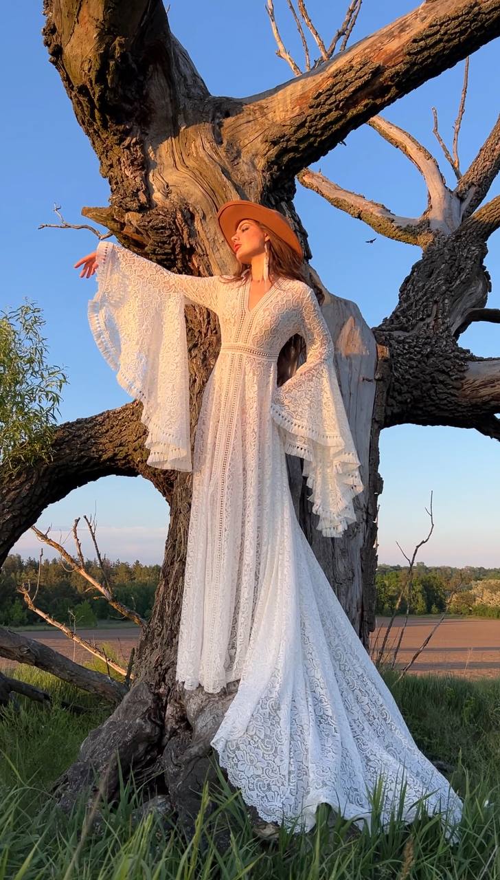 a woman in a white dress and hat standing in front of a tree