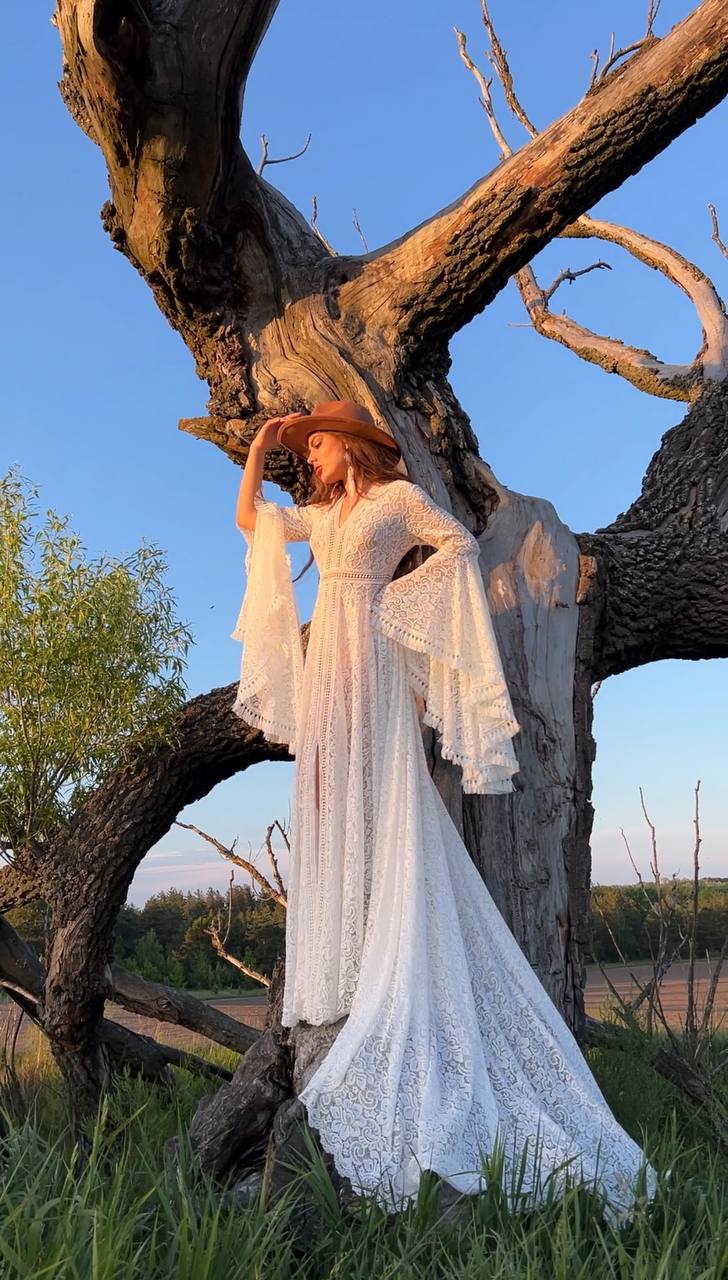 a woman in a white dress and hat standing in front of a tree